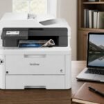 Brother MFC-L3780CDW color all-in-one printer on a premium home-office desk beside a laptop