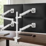 White Ergotron LX Quad monitor arm holding four 24-inch class office monitors in a 2x2 grid on a walnut home-office desk