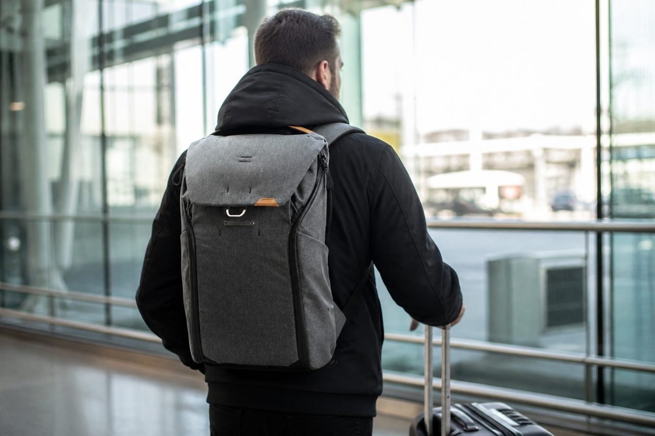 Photographer wearing the Peak Design Everyday Backpack 30L Charcoal through an airport terminal with a roller bag