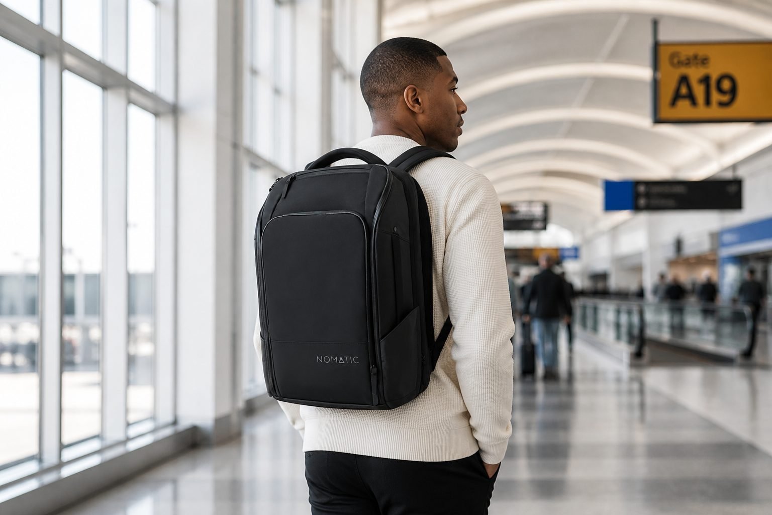 Traveler wearing the NOMATIC 20L Travel Pack Black through an airport concourse