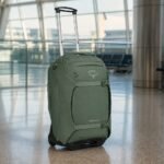Osprey Sojourn Wheeled Travel Pack 22/45L in Koseret Green standing in an airport terminal with telescoping handle extended