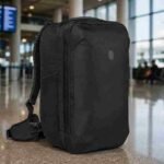 Tortuga 40L Travel Backpack Lite in Black standing in a premium international airport terminal