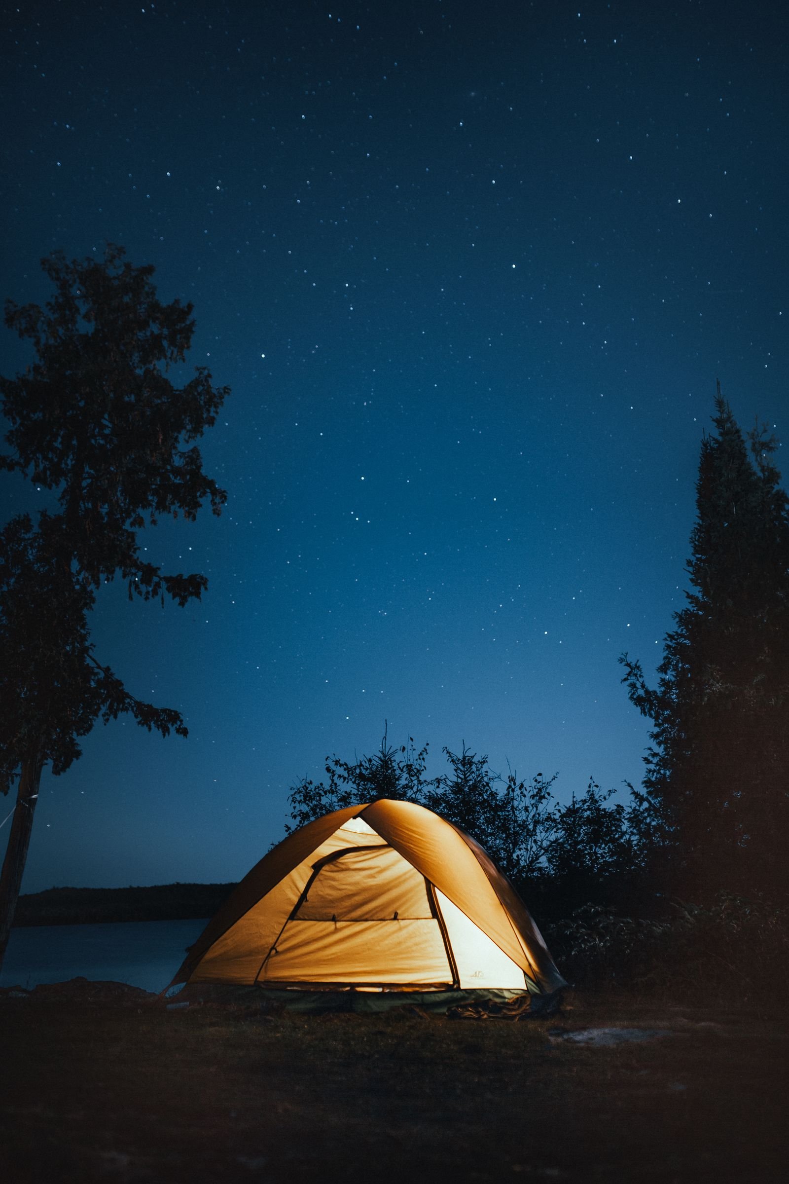 Lit tent beside a lake at night